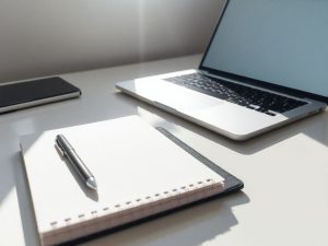 Birou ordonat cu laptop deschis și caiet, luminat natural.